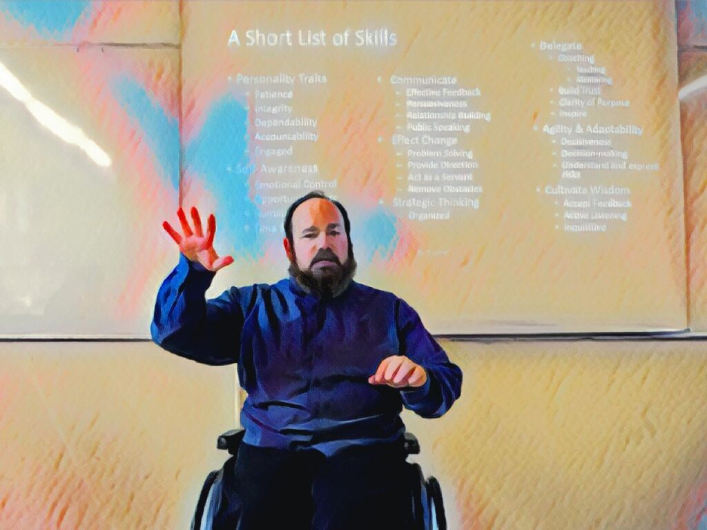 Cartoonish photo of Dr. D. sitting in his chair, right arm outstretched fingers extended dramatically, talking about Leadership Skills. A "Short list of Skills" is on the board behind him.